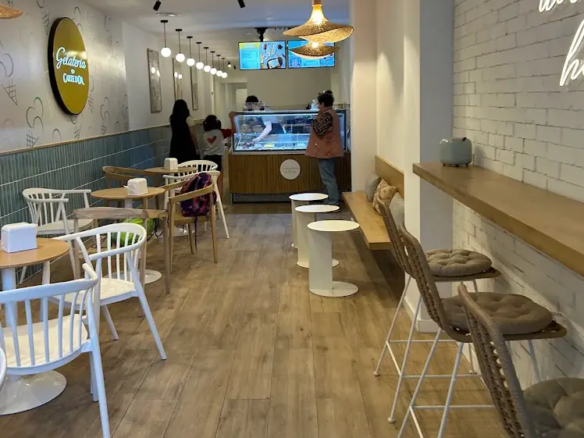 Interior moderno y luminoso de la cafetería heladería en traspaso en la calle Lesseps, Barcelona, con clientes en el mostrador.